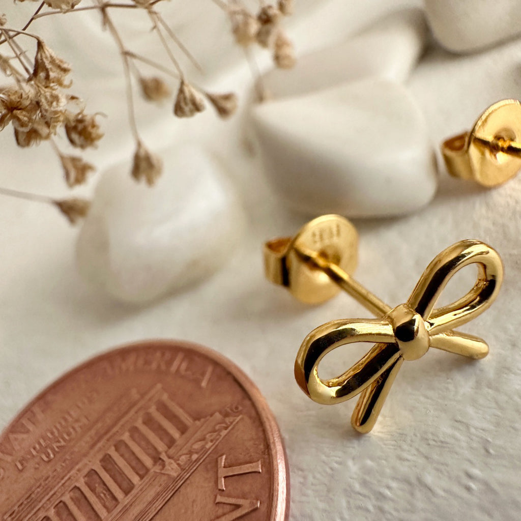 Bow Stud Earrings Gold besides a penny.