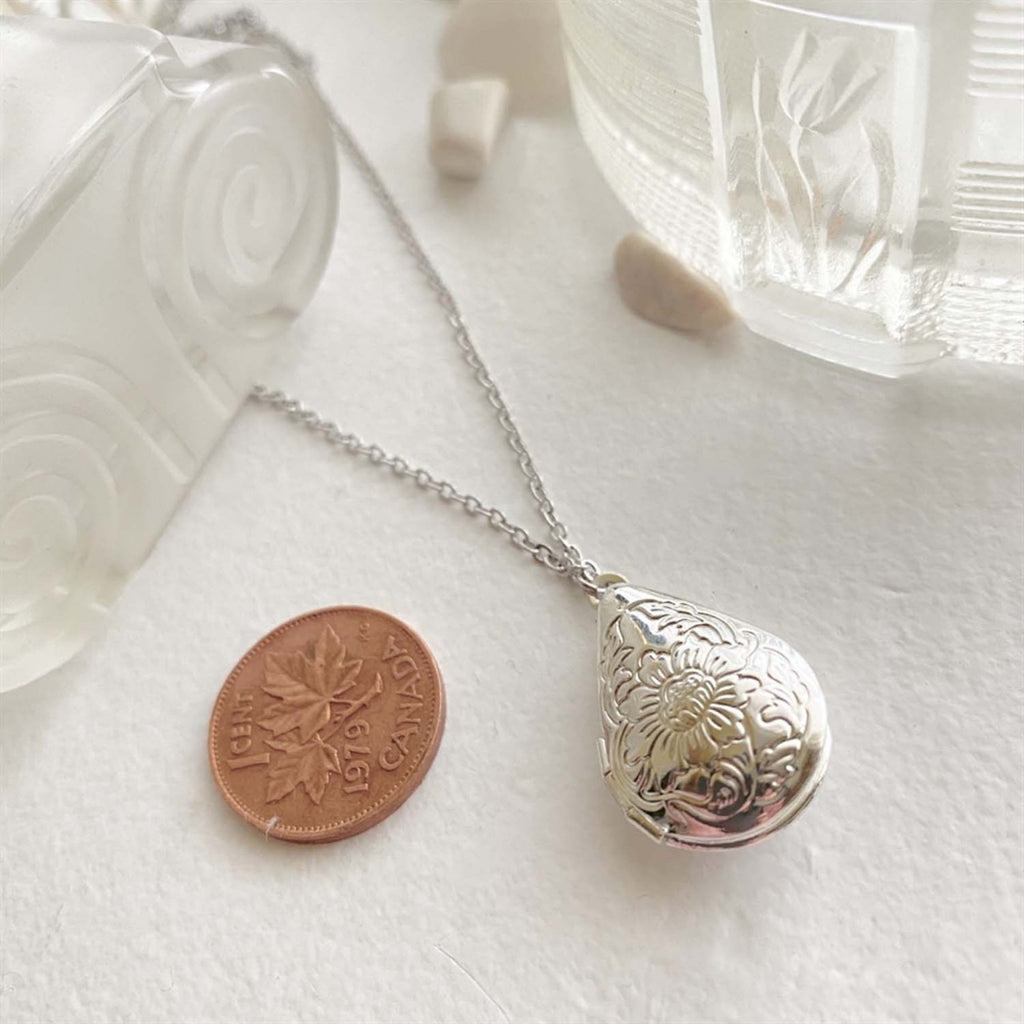 Floral Design Teardrop Locket Necklace Silver besides a penny.