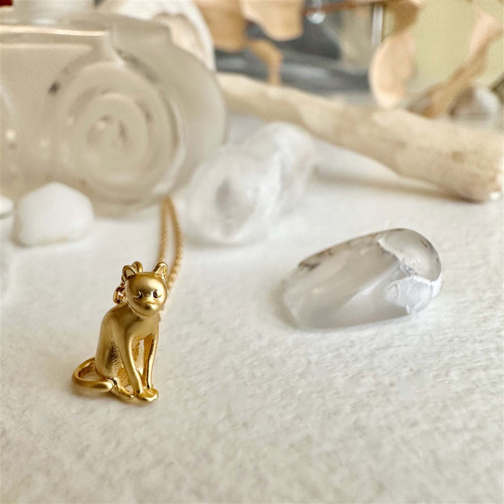 The Thinking Cat Charm Necklace Gold on table.