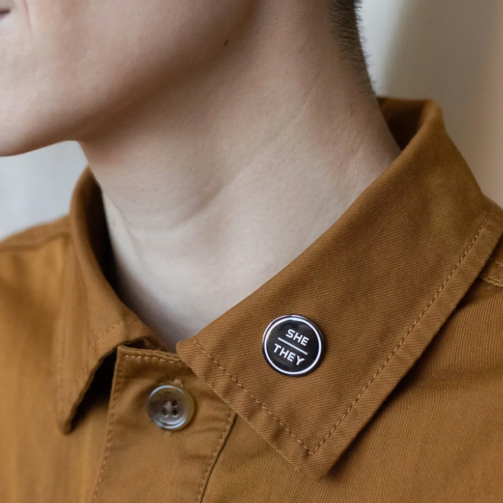 Anthracite Enamel Pronoun Pin: She/They Person wearing.