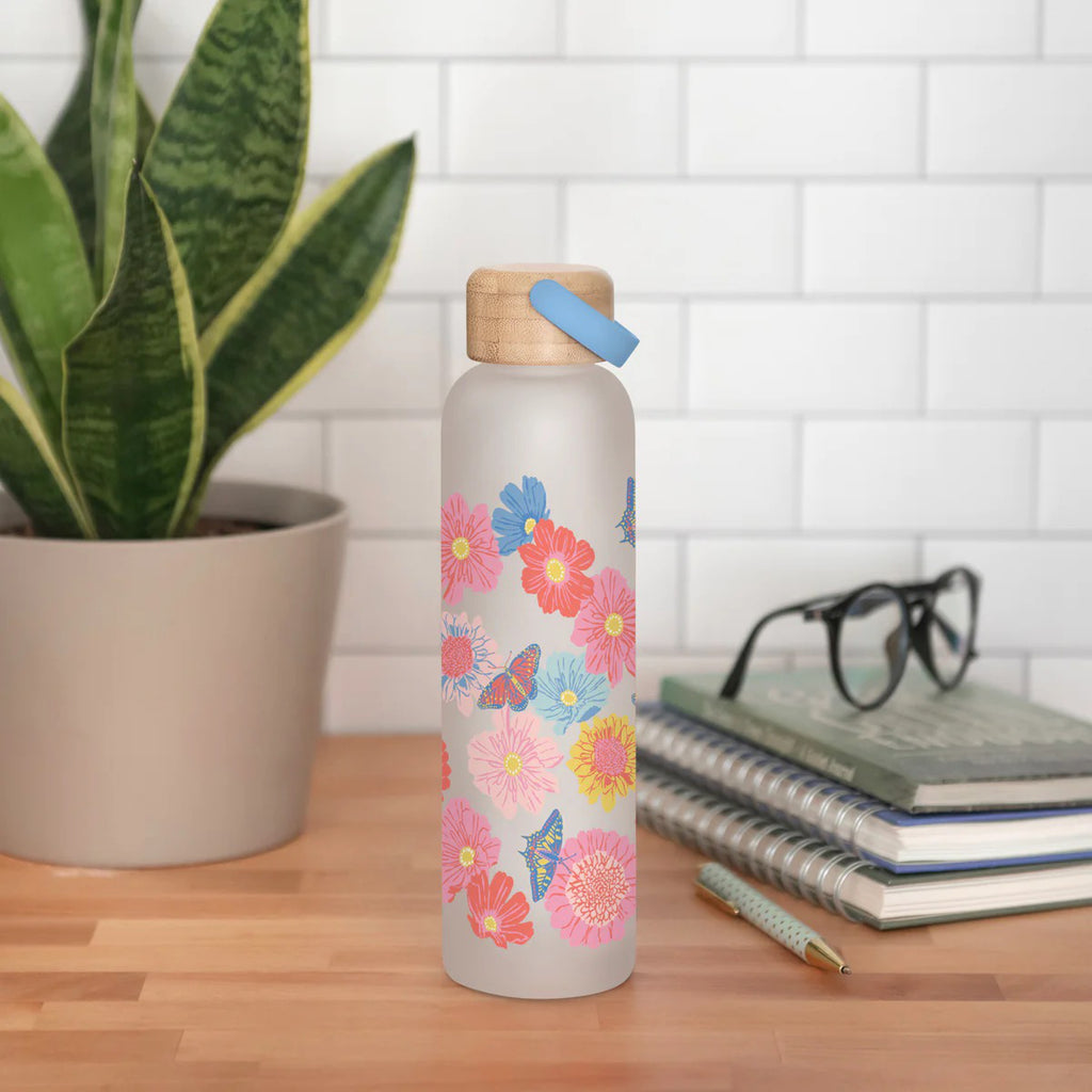 Butterfly Blossoms Glass Water Bottle with Bamboo Lid on table.