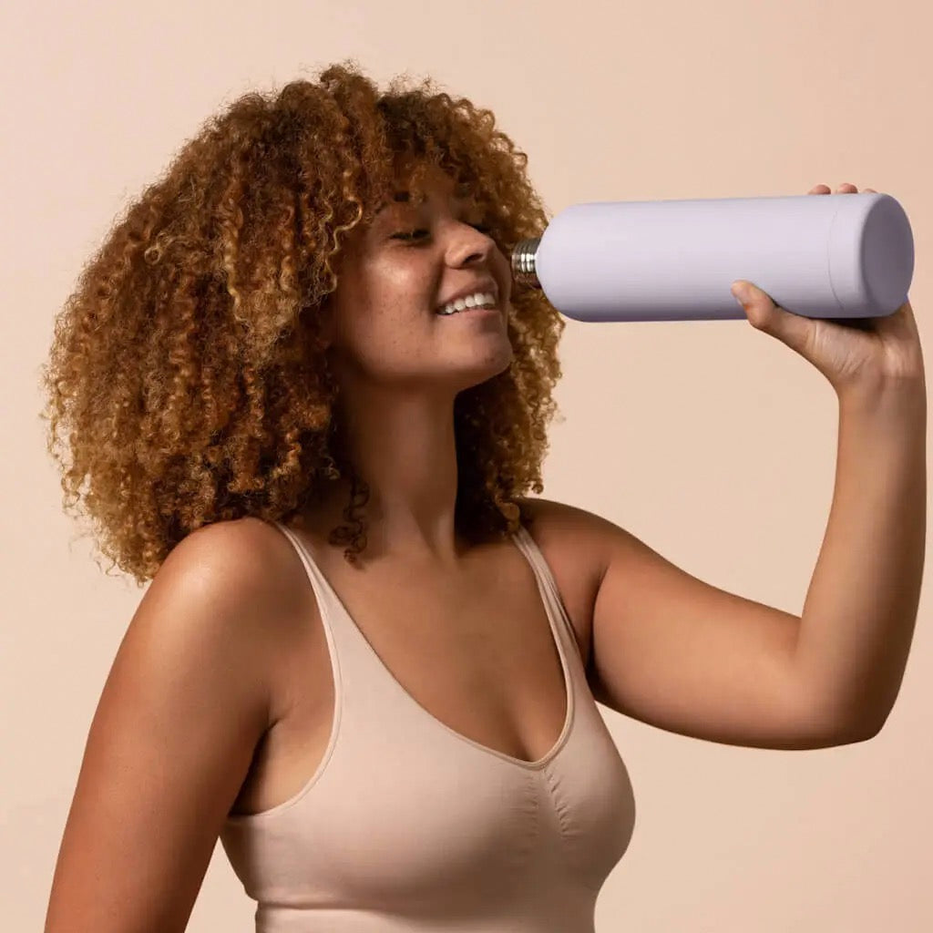 Woman drinking from Beysis mauve water bottle.
